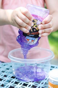 a child is pouring purple liquid into a plastic container on top of a metal table