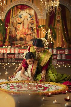 a woman and child sitting on the floor in front of a decorated mat with candles