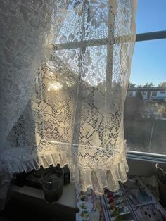 an open window with white lace curtains and magazines on the windowsill, in front of a sunny blue sky