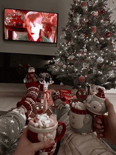 two people are holding cups in front of a christmas tree with lights and decorations on it