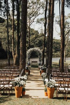 an outdoor ceremony set up with chairs and flowers in large flower pots on the aisle