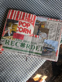 a person holding up a newspaper with the word pop corn written on it in front of them