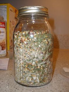 a glass jar filled with lots of green stuff next to a carton of cereal