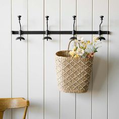 a basket with flowers hanging from it on a wall next to a chair and coat rack