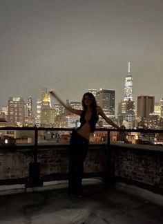 a woman standing on top of a roof in front of a city skyline at night