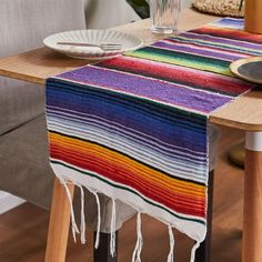 a colorful table runner with tassels and plates on the table next to it