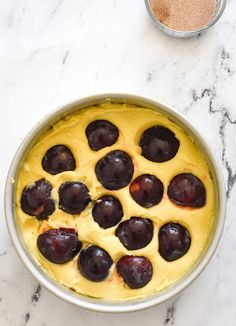 a pan filled with batter and cherries on top of a marble counter next to a measuring cup