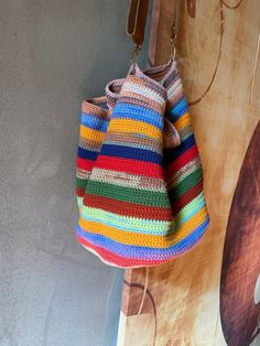 a multicolored crocheted bag hanging from a hook on a wooden wall