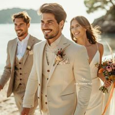 a man in a suit and tie walking with two women on the beach next to him