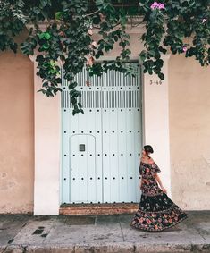 a woman standing in front of a blue door with vines growing over the top and bottom