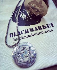 a white shirt with a black market logo on it and a silver necklace hanging from the front