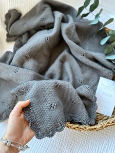 a person holding up a gray scarf in front of a basket with eucalyptus leaves on it