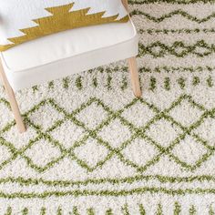 a white chair sitting on top of a rug next to a green and white pillow