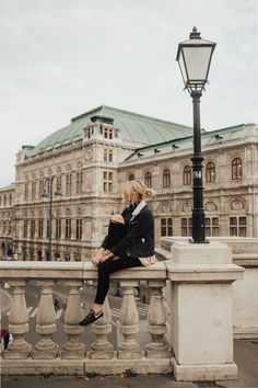 a woman sitting on top of a stone bench next to a lamp post and building