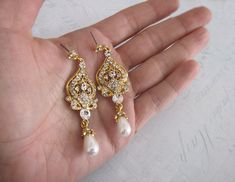 a hand holding two pairs of gold and pearl earrings