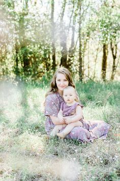 a woman holding a baby in her arms while sitting on the ground near some trees