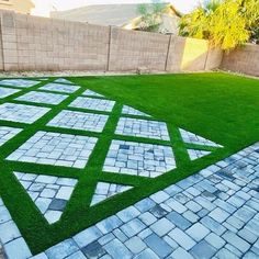 an artificial grass lawn in a backyard with white and gray tiles on the ground, next to a brick wall