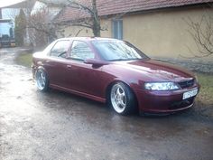 a maroon car parked in front of a house on a wet driveway next to a tree