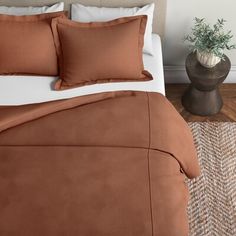 a bed with brown sheets and pillows in a room next to a potted plant