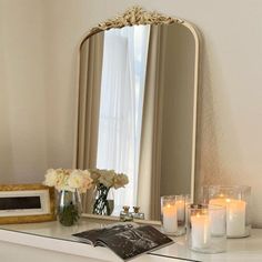 a mirror sitting on top of a white dresser next to candles and flowers in vases