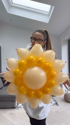 a woman holding balloons in front of her face and looking at the camera while wearing glasses