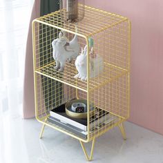 a yellow wire shelf with two white rabbits on it and a pink wall in the background