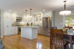 a kitchen and dining room with hardwood floors, white cabinets and stainless steel refrigerator freezer