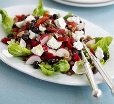 a white plate topped with a salad covered in feta cheese and cherry tomatoes on top of a wooden table