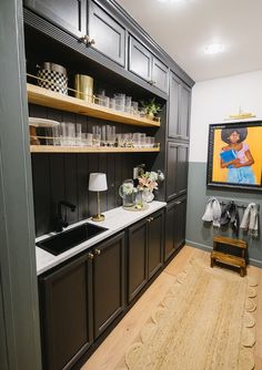 a kitchen with black cabinets and white counter tops, wooden flooring and an art piece on the wall