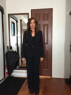 a woman standing in front of a mirror wearing a black suit and heels with her hands on her hips