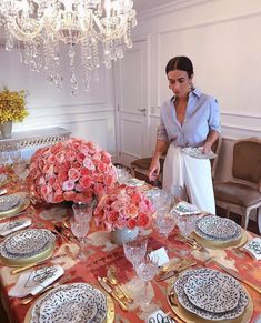 a woman setting a table with plates and flowers