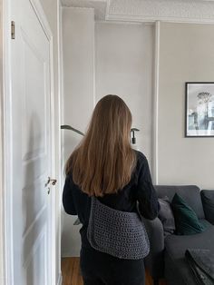 a woman standing in front of a couch with a crocheted purse on her back