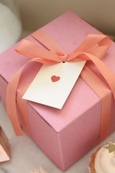 a pink box with a tag on it and some cupcakes in the background