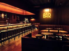 a dimly lit bar with several stools and tables in front of the bar area