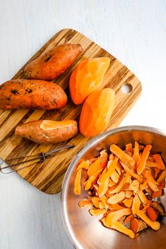 carrots and sweet potatoes on a cutting board next to a metal bowl with spoon