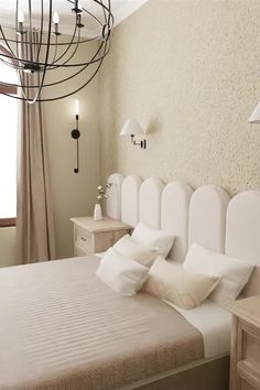 a white bed sitting next to a window with curtains on the windowsill and a chandelier hanging above it