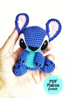 a hand holding a small blue crocheted stuffed animal with ears and eyes,