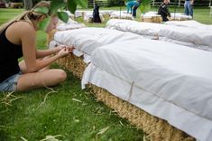 a woman sitting on the ground next to hay bales with white sheets laid over them