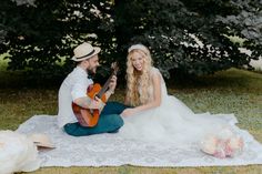 a man and woman are sitting on the ground playing guitar together in front of some trees