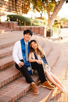 a man and woman are sitting on the steps together in front of some stairs with trees