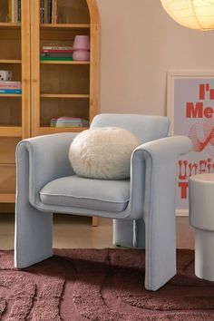 a blue chair with a white pillow sitting on top of it next to a book shelf