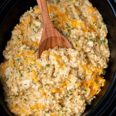 a wooden spoon in a slow cooker filled with rice and cheese, ready to be cooked