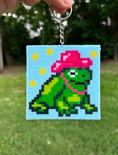 a hand holding a pixel art keychain in the shape of a turtle wearing a pink hat