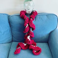 a crocheted scarf sitting on top of a blue couch next to a glass head