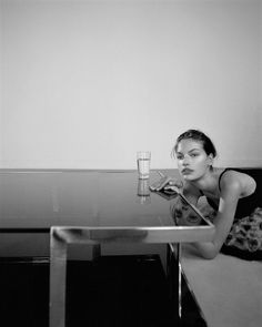 a woman sitting at a glass table with a drink in her hand and looking into the camera