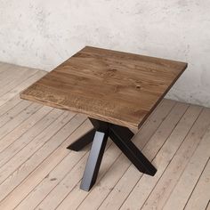 a square wooden table with metal legs on a hard wood floor in front of a white wall