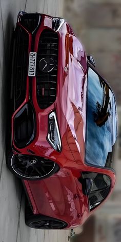 the front end of a red sports car parked next to a wall with its hood up