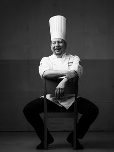 black and white photograph of a smiling chef sitting on a chair with his arms crossed