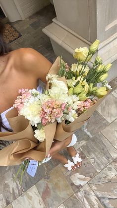 a woman holding a bunch of flowers on top of a tiled floor next to a building