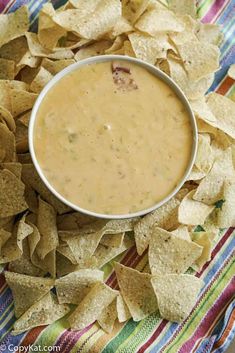 a bowl of dip surrounded by tortilla chips on a colorful cloth with a striped napkin